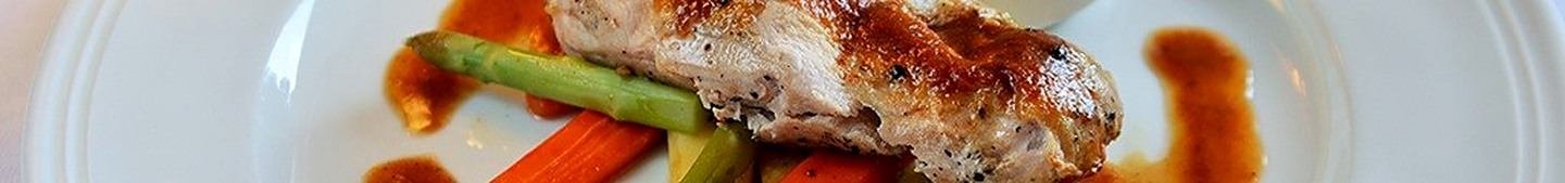 A close panoramic crop of a plated main course finished with a glossy jus.